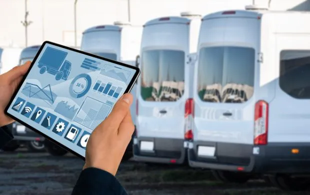 Fleet manager holding tablet with telematics platform on display and their minibus fleet in the nackground
