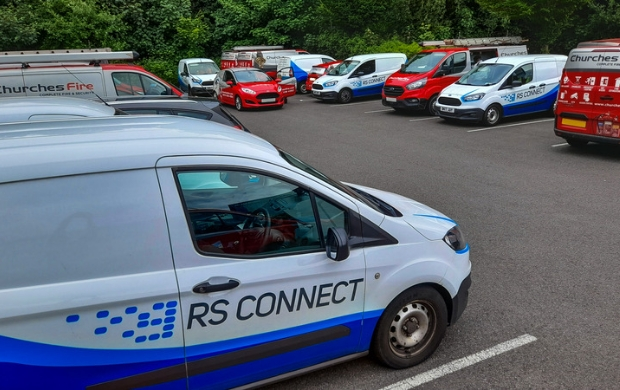 engineers installing vehicle trackers on a fleet of commercial vehicles parked in a car park.