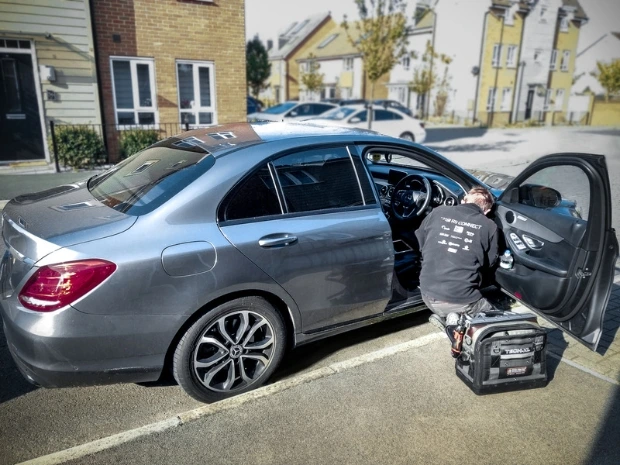 RS Connect engineer fitting an Autowatch Ghost immobiliser to a grey Mercedes C Class car outside a customer's address.

