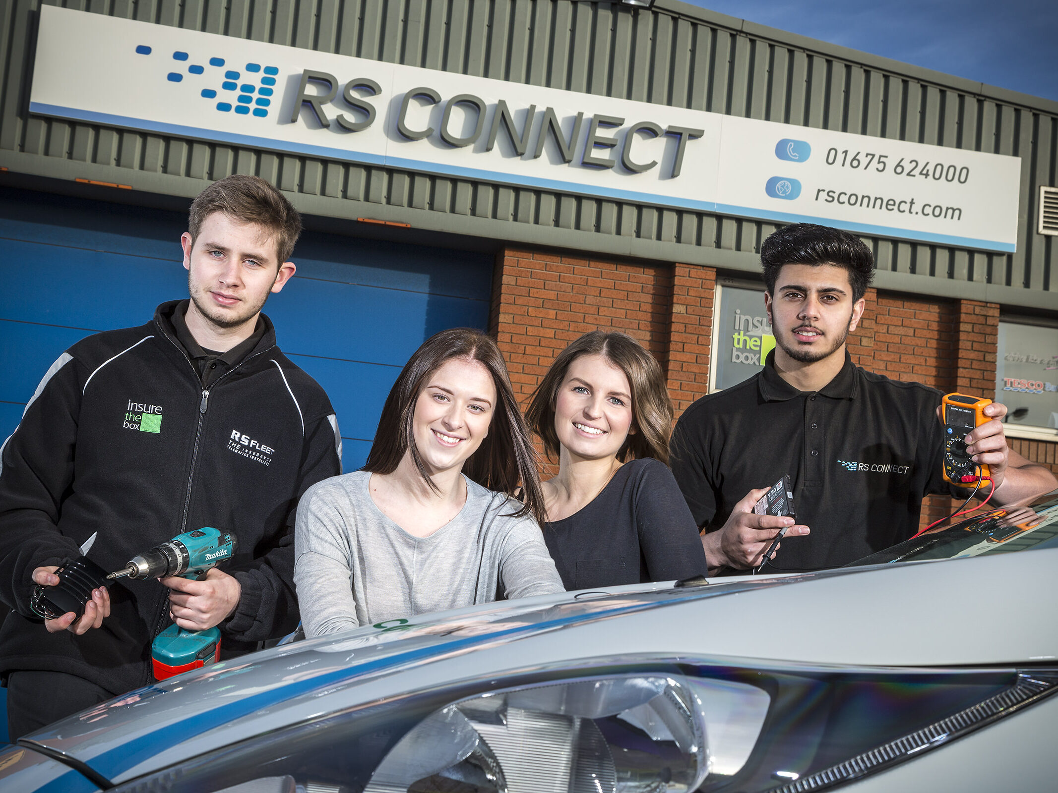 Photograph showing exterior of RS connect premises with four young people. The apprentices are holding tools to demonstrate the installations process.